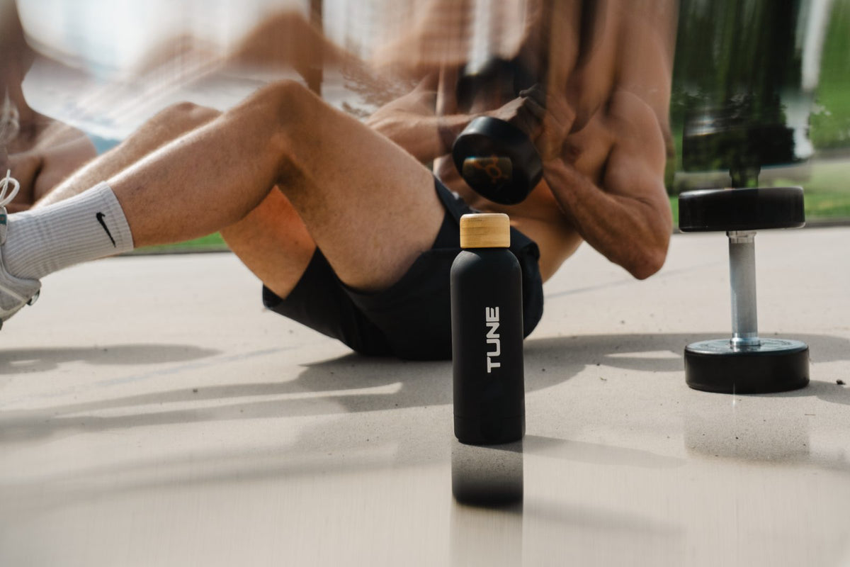 Black Tune bottle on a gym floor next to a dumbbell
