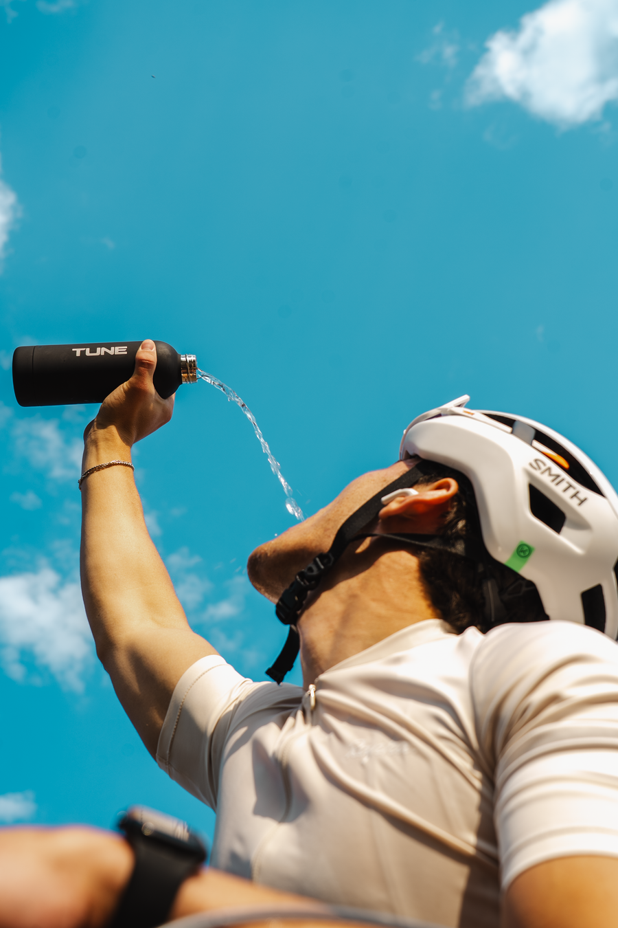 A cyclist drinking from a Tune bottle under a clear blue sky