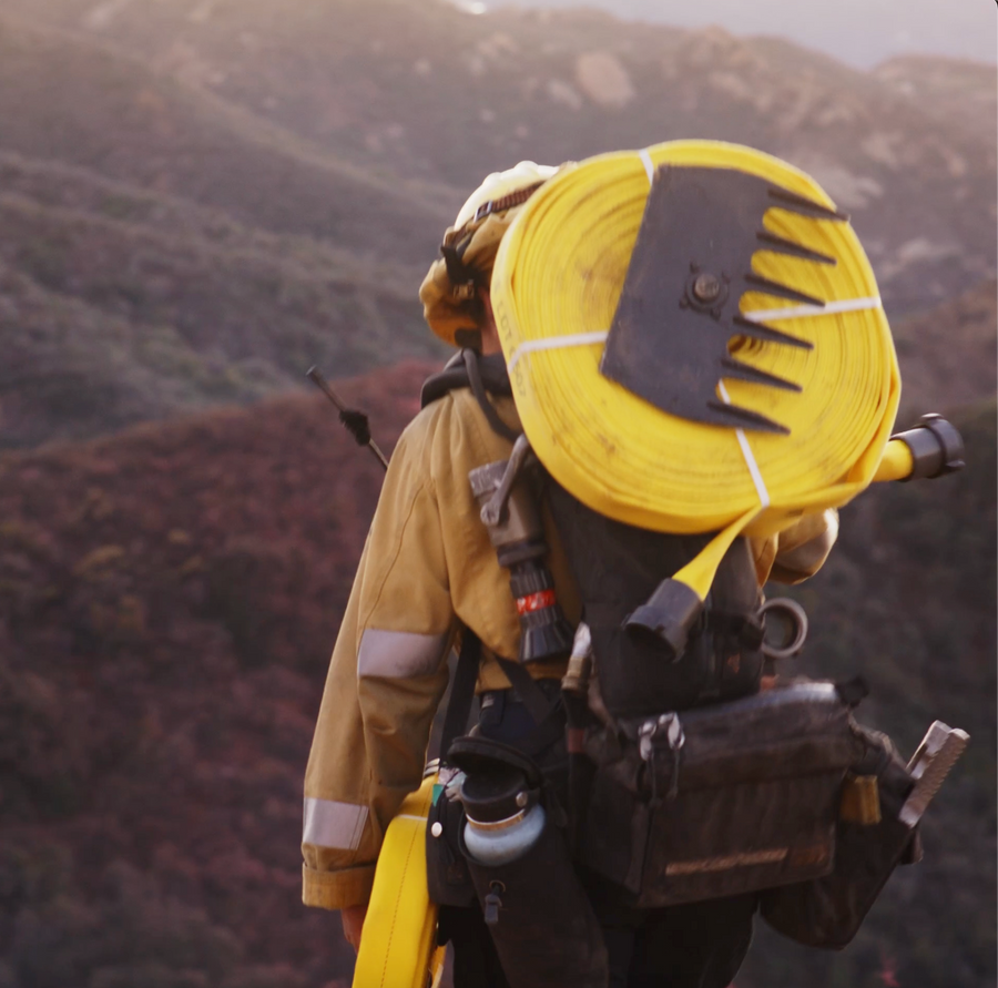 Wildland firefighter carrying hose up a hillside