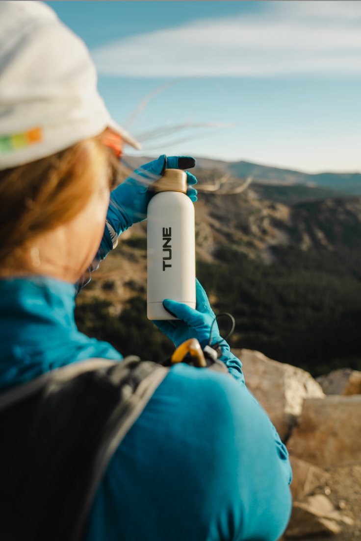 Hiker on a mountain ridge holding a Stone Tune bottle